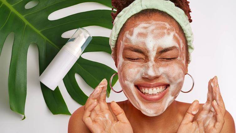 Beautiful woman washing face with green leaf and cleanser in the background